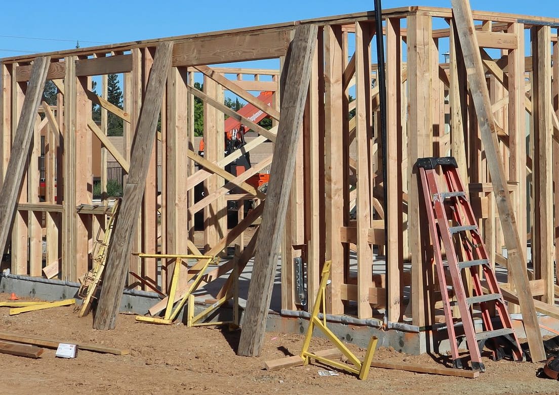 Bare wood stud walls on a new-build lot, with a ladder inside. Crew photo, credited on the credits page.